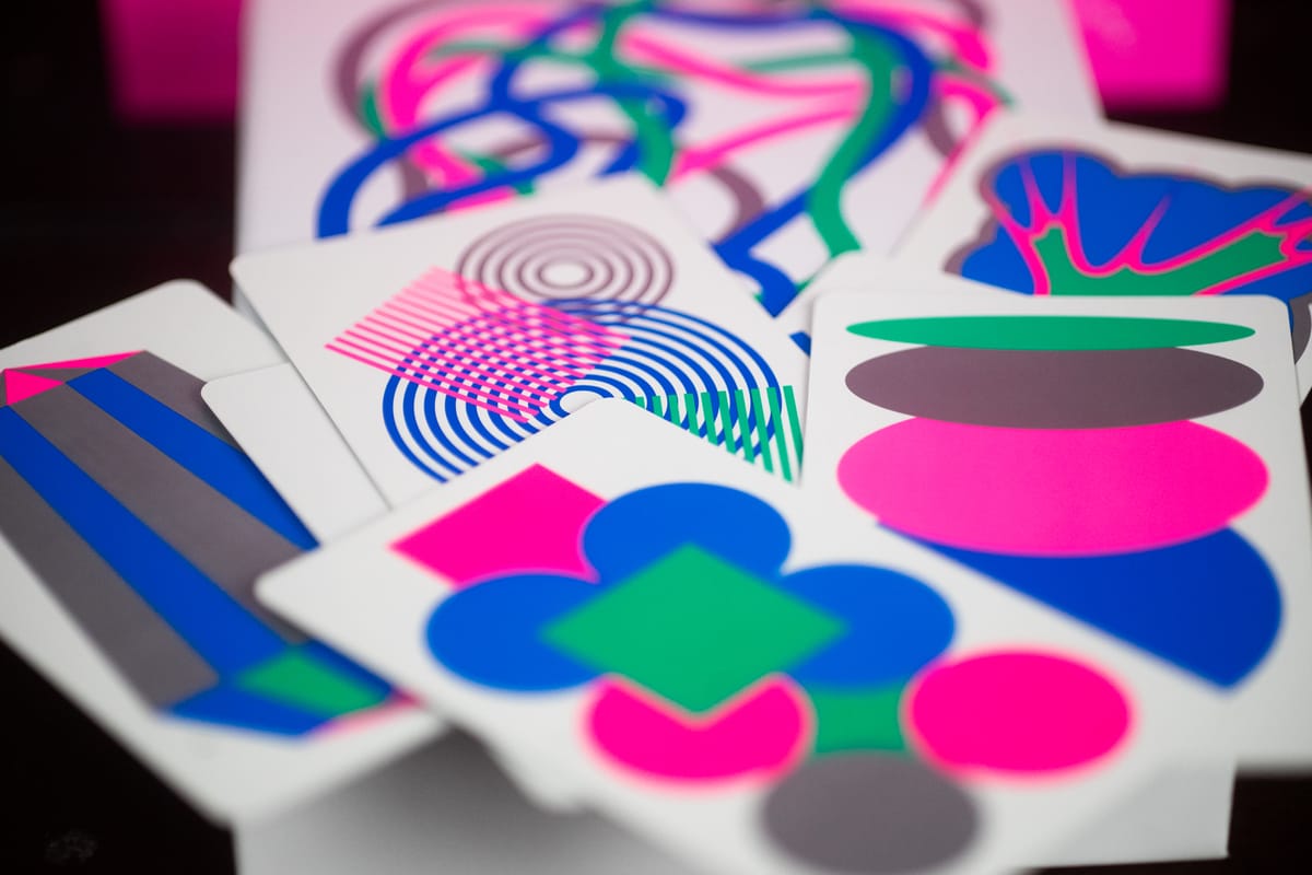 Cards from the game Figment displayed on a table. They are brightly colored with magenta, blue, green and silvery-gray colors.