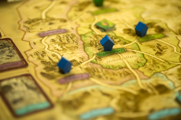 The game Thurn and Taxis in play, with three blue wooden houses on a board. The town of Sigmaringen in a map of Germany is in focus.